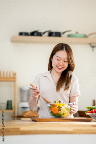 An Asian woman is making a salad in the kitchen. The concept is related to healthy eating and dieting.
