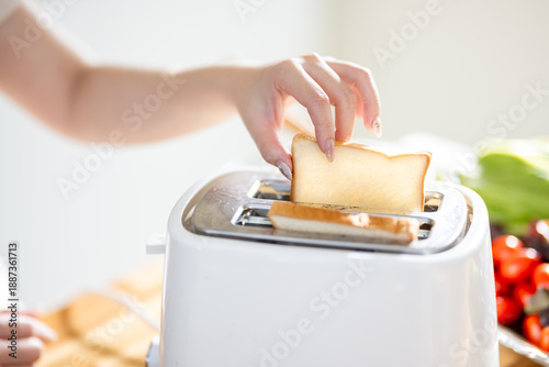 An Asian woman is happily toasting bread for breakfast in the kitchen.