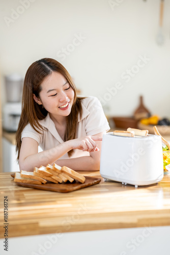 An Asian woman is happily toasting bread for breakfast in the kitchen.