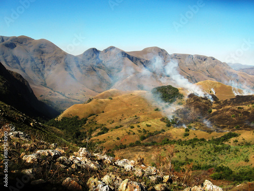 A small wildfire burning in the grasslands of the Baberton-Mokhonjwa Mountains on a clear sunny day.