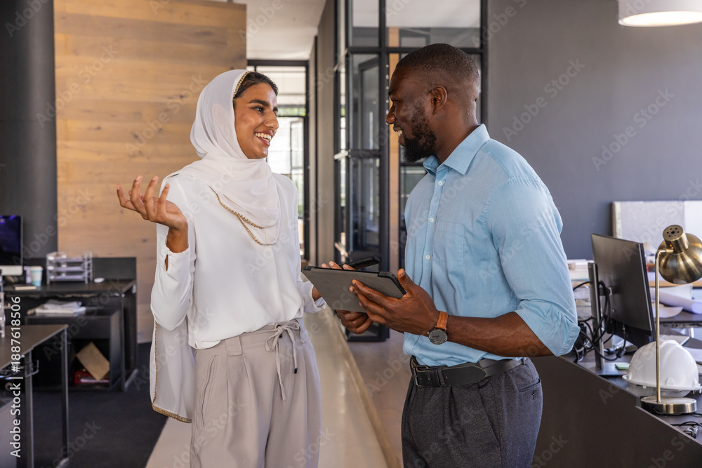 Fototapeta premium Diverse coworkers in business attire discussing plans on tablet next to white hardhat in office