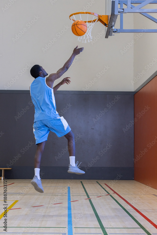 Obraz premium Male basketball player performing layup toward hoop inside gymnasium on court with lines