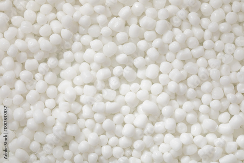 Fotografie A top-down macro photo shows a dense, uniform collection of polymer granules, bright white and with a smooth matte finish