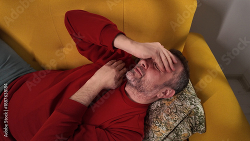 Принти на полотні Man with headache, depression, sadness and loneliness sitting on a couch at home