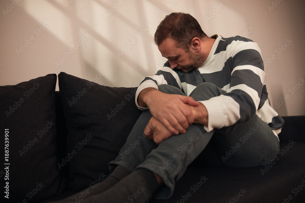 Fototapeta premium Man with headache, depression, sadness and loneliness sitting on a couch at home.