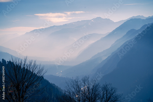 Soft blue himalaya mountain ridges fading into mist, calm natural landscape with silhouette of bare trees foreground in Manali, kullu, Kashmir India