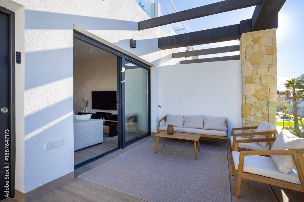 Obraz premium Sunny apartment terrace with outdoor lounge furniture and modern glass sliding doors