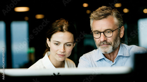 Two people working together on a computer in an office setting.