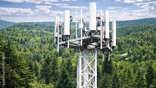 Telecommunication tower with cellular antennas for 5g mobile internet network against a clear blue sky with a forest in the background.
