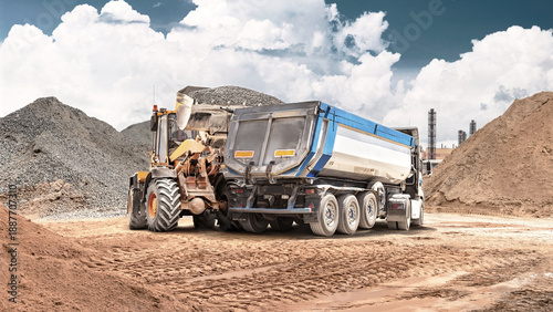 Slika na platnu At a construction site, a wheel loader loads sand into a nearby dump truck using its bucket