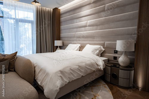 Bilde på lerret A king bed with white linens sits before suede like headboard panels, woven wood columns, ceramic lamps, and sheer drapes, with a curved sofa edge and patterned rug
