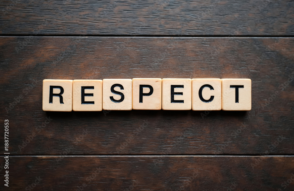 Naklejka premium Wooden blocks spell the word RESPECT on a dark wood surface. Concept conveys acknowledgement honor and regard for others. Simple graphic text.