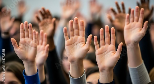 Upward reaching hands of young adults in a lecture hall showing active engagement and participation in a discussion