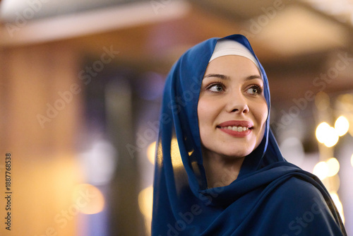 Smiling Woman in Blue Hijab Outdoors at Night With Warm City Lights Behind