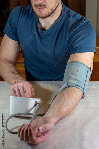 Man using a digital blood pressure monitor at home. Close up of a person sitting at a table with an automatic arm cuff for health monitoring, hypertension prevention and medical self-diagnostic.