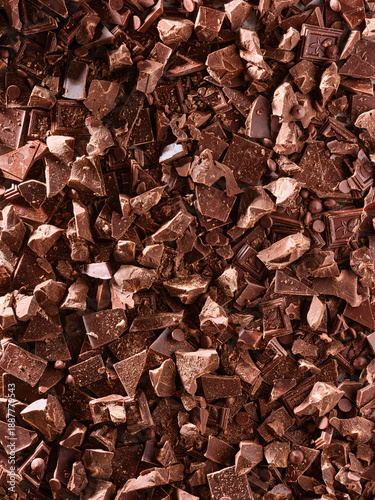 Different sizes of chocolate chunks and pieces are spread over a flat surface. These pieces are used for baking and cooking in various recipes