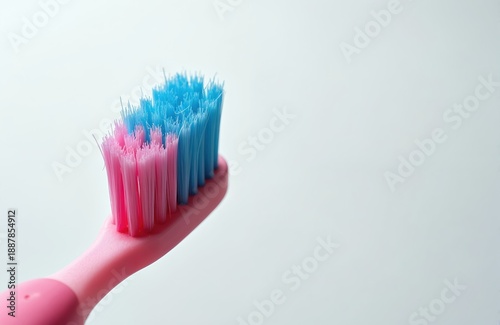 Close-up view of pink toothbrush with blue, pink bristles on clean white background. Object is isolated for use in dental hygiene or healthcare content. Brushing teeth daily ensures good oral health. © Vadym