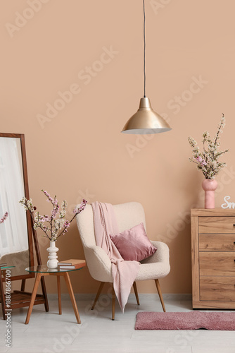 Armchair with dresser, mirror and vases of blooming branches near beige wall in living room