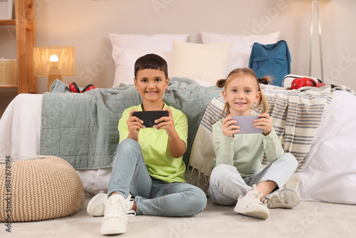 Cute happy little kids with mobile phones playing video games on floor at home