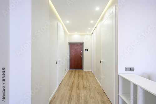 Modern hallway with light wooden flooring, white walls, recessed ceiling lights, built-in shelving, closed white doors, burgundy entrance door, minimalist design.