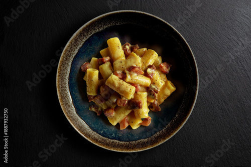 Dark bowl with rigatoni pasta carbonara on black stone