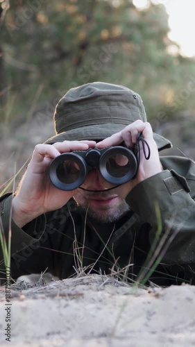 A reconnaissance battalion soldier observes the enemy through binoculars while hidden in the forest. Vertical video format.