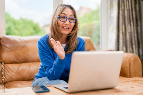 Woman talks on laptop from her living room during a video call in the afternoon Free Download Woman talks on laptop from her living room during a video call in the afternoon - GFXLoad