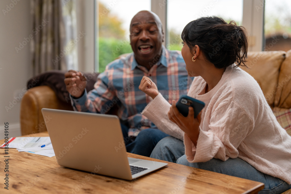 Obraz premium Two people engage in lively discussion at home while seated on a couch with a laptop