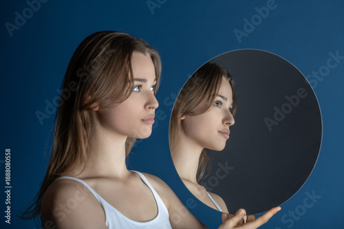 Young woman looking at her profile in a circular mirror against a blue background