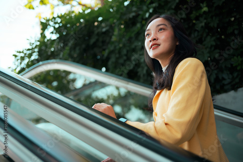 Fotografie Asian woman moving up escalator looking optimistic