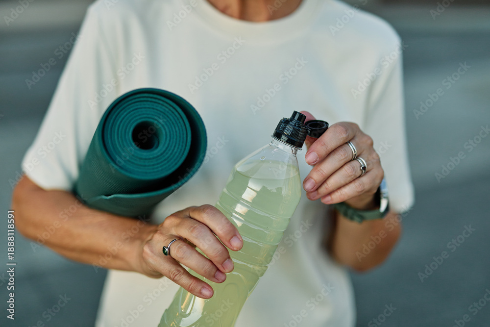 Obraz premium Portrait of a middle aged mature beautiful sport woman smiling happy and confident. Standing and doing exercise and stretching and holding a bottle of water or energy drink or juice during a break in