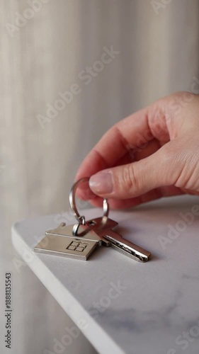 Female hand laying down key with house keychain on table, real estate and property ownership.