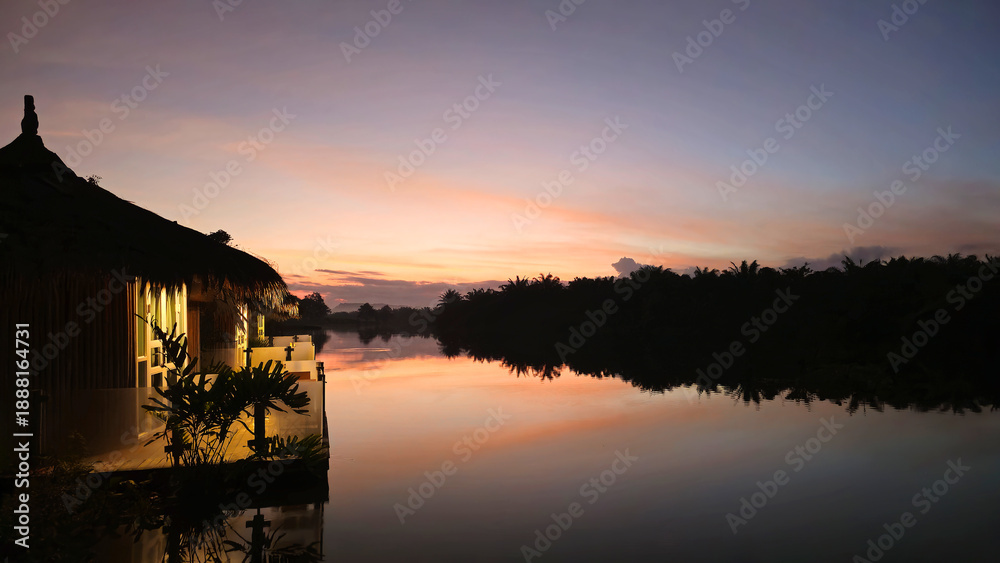 Obraz premium Resort bungalows reflecting colorful sunrise sky over River Tha Sathon, Surat Thani, Thailand, Southeast Asia.