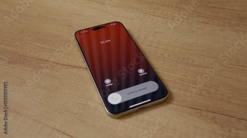 A smartphone receives an incoming call labeled as scam while placed on a wooden table. The call is a reminder to stay alert about potential dangers of phone scams.