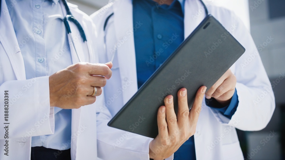 custom made wallpaper toronto digitalClose view of two doctors standing outside clinic. Medical specialists using tablet while reviewing symptoms. Focus on coordinated teamwork. Hands pointing at screen during case evaluation.