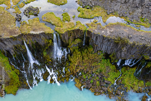 Sigoldugljufur canyon, Iceland Highlands. Crystal-clear waterfalls pour from mossy lava walls into a vibrant turquoise blue river winding through volcanic terrain.