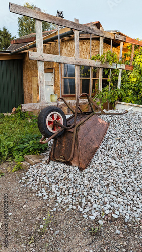 Wallpaper Mural Old metal wheelbarrow tipped on gravel in front of rustic farmhouse and shed, warm evening light, quiet renovation mood Torontodigital.ca