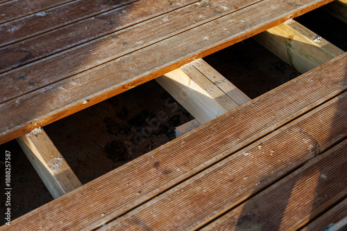 Tableau sur toile Wooden deck section shows removed planks, fresh light joists, sawdust, ridged boards, screw holes, and clean joinery, in warm late afternoon light on a residential deck