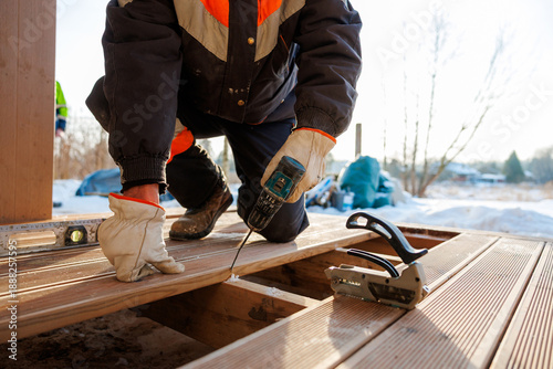 Fotografi A deck installer kneels on joists, driving a screw with a cordless drill into composite boards