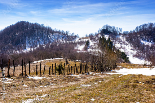 rural landscape of carpathian mountains in early spring under blue sky. snow covered hill with barbed wire fence on sunny day. green environment sustainability and protection. background for earth day