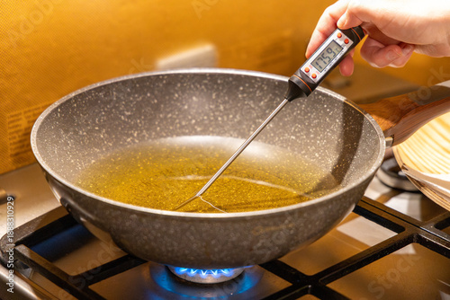 Checking cooking oil temperature with digital thermometer in frying pan on gas stove for perfect deep frying doughnuts and professional culinary food preparation concept.