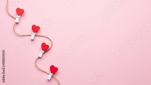 Valentine's Day A close-up, top-down view of red heart-shaped objects clipped onto a rope with wooden clothespins against a pink background, evoking a sense of love and affection