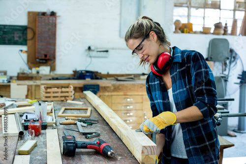 Slika na platnu Female woodworker wearing safety goggles and gloves planing long timber at shop