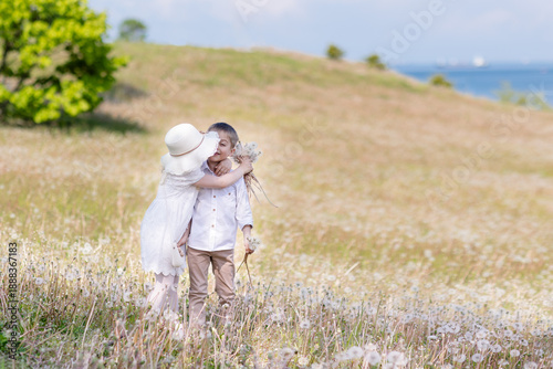 A little girl is hugging a boy on a sunny lawn with dandelions.