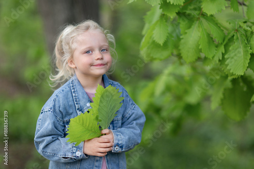 A little girl with green oak leaves in her hands is smiling at the camera.