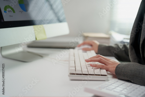 Professional hands typing on a modern white keyboard while working on a desktop computer in an office, managing data and business analysis with reports on screen