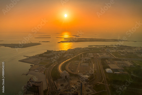 Aerial view of Abu Dhabi, UAE, including Qasr Al Watan and the Corniche. Coastal urban development meets the Persian Gulf during sunset glow.
