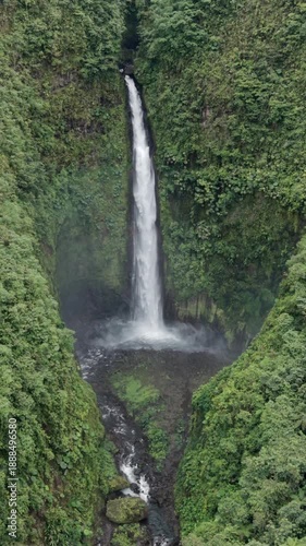 Drone push in with gimbal tilt toward tall waterfall in tropical rainforest
