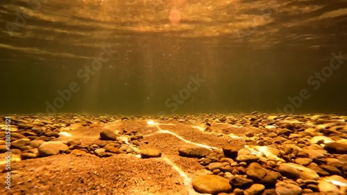 Sunlight Refracting Through Clear Water Illuminating a Pebble and Sand Underwater Scene