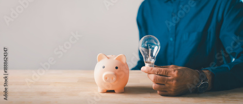 Tableau sur toile Man holding light bulb next to piggy bank for financial innovation, money saving